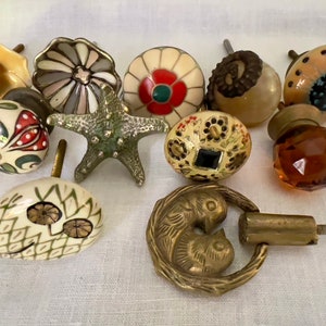 May include: Assortment of 11 decorative cabinet knobs in various styles and colors.  The knobs feature floral, geometric, and animal designs.  Some knobs are made of ceramic, while others are made of metal.