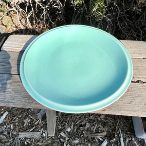 May include: A light blue ceramic serving dish or platter. The dish is round and has a slightly raised rim.
