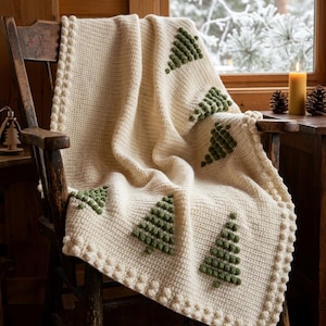 May include: A cream-colored crocheted blanket featuring a repeating pattern of raised green textured pine tree motifs. The blanket is finished with a decorative bobble stitch border along all edges, creating a tactile and uniform appearance.