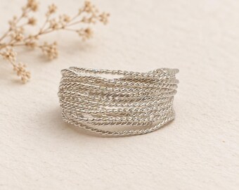 May include: A wide silver ring constructed from multiple thin, twisted metal strands layered together to create a textured, multi-band appearance. The design features a continuous, interwoven pattern of metallic rope-like wire in a bright finish.