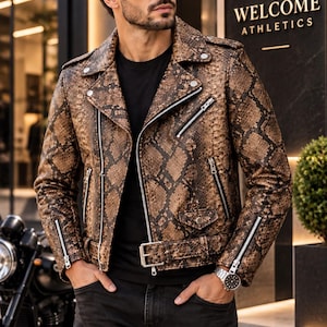 Puede incluir: Una chaqueta de moto de cuero con estampado de piel de serpiente en marrón y negro, con cremalleras metálicas plateadas, solapa con muescas, cinturón con hebilla metálica y detalles de botones a presión en el cuello y un bolsillo frontal.