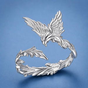 May include: A silver-colored open ring featuring a detailed bird design with spread wings and a long, curved tail. The metal surface has a polished finish, and the inner band is clearly stamped with the text S925, indicating the metal composition.