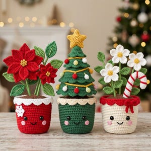 May include: Three crocheted potted plants featuring a red poinsettia, a green Christmas tree with a yellow star, and white flowers with a candy cane. Each pot has a smiling face with black eyes, a stitched mouth, and pink cheeks.
