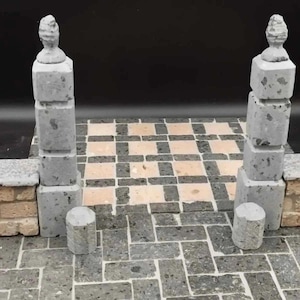 Peut inclure: Un modèle architectural miniature présentant deux grands piliers en pierre grise surmontés de fleurons, encadrant une allée pavée. Le sol est composé de dalles rectangulaires alternant entre le beige clair et le gris foncé.