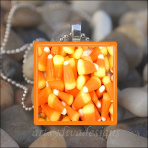 May include: Orange and white candy corn in a square orange frame. The frame is attached to a silver chain.