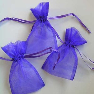 May include: Three purple organza gift bags with drawstrings. The bags are made of sheer fabric and have a delicate, feminine look.