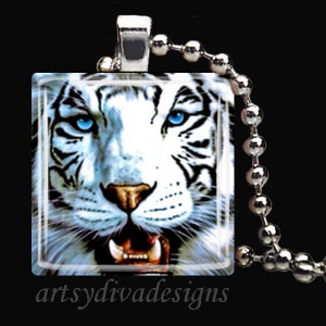 May include: A white tiger with blue eyes is featured on a square glass pendant. The pendant is attached to a silver chain.