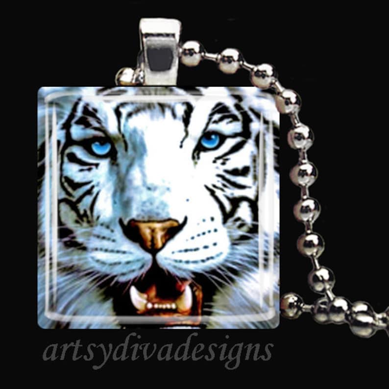 May include: A white tiger with blue eyes is featured on a square glass pendant. The pendant is attached to a silver chain.