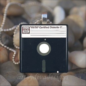 May include: A black and white floppy disk necklace with a silver chain. The disk is labeled "Radio Shack Certified Diskette" with a blank space for the disk number.