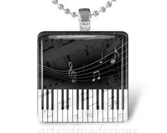 Puede incluir: Un collar de cadena de plata con un colgante de vidrio blanco y negro que presenta un teclado de piano y notas musicales. El colgante tiene forma cuadrada.