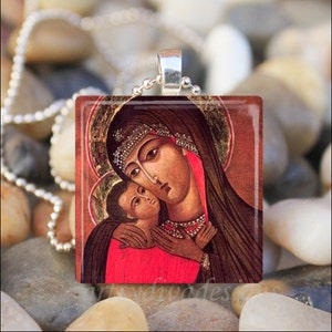 Puede incluir: Un colgante de vidrio con un icono religioso de la Virgen Mar&iacute;a sosteniendo al ni&ntilde;o Jes&uacute;s. El icono est&aacute; pintado en un estilo tradicional con detalles dorados y un fondo rojo.