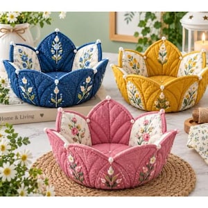 May include: Three fabric bowls shaped like lotus flowers, featuring quilted textures and floral embroidery. One bowl is deep blue, one is mustard yellow, and one is rose pink. Each petal is accented with a small white bead at the top edge.