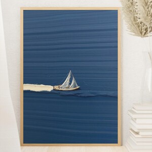 Könnte beinhalten: Ein gerahmter Wandkunstdruck mit einem texturierten, tiefblauen Hintergrund mit horizontalen Pinselstrichen. Ein kleines Segelboot mit weißen Segeln ist mittig platziert und hinterlässt eine dicke, texturierte weiße Spur im Wasser.