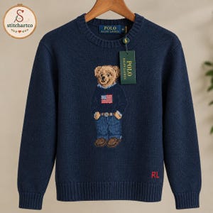 Könnte beinhalten: Ein dunkelblauer Langarmpullover mit Rundhalsausschnitt und einem Strickmotiv eines Teddybären, der einen Pullover mit amerikanischer Flagge, eine blaue Jeans und braune Schuhe trägt. Der Pullover zeigt den Schriftzug POLO RALPH LAUREN.