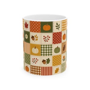 Puede incluir: Una taza de cerámica blanca con un patrón de mosaico repetitivo de cuadrados con temática otoñal. El diseño incluye ilustraciones de calabazas naranjas, calabacines verdes, bellotas marrones, hojas de arce rojas y bayas, intercaladas con cuadros de lunares, rayas y cuadros.