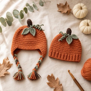 May include: Two orange crochet hats shaped like pumpkins. One hat features ear flaps with braided tassels in orange, green, and brown yarn. Both hats are topped with a brown stem and two green leaves. The hats are made of textured yarn stitches.