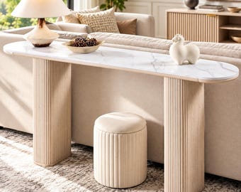 May include: A long, narrow console table with a white faux marble top and two light-colored, vertically fluted cylindrical bases. A matching fluted, round ottoman sits underneath the table between the two bases.