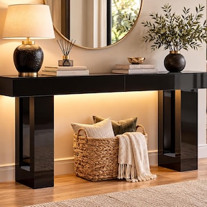 May include: A long, black, high-gloss console table with integrated under-shelf lighting. The table features two thick, rectangular legs and a flat top surface. A woven wicker basket containing two pillows and a cream-colored throw sits below.