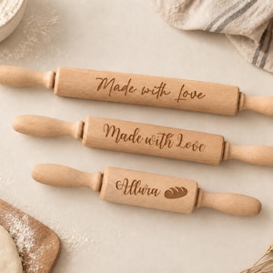May include: Three light brown wooden rolling pins of varying lengths. The two larger rolling pins are engraved with the text Made with love. The smallest rolling pin is engraved with the text Allura and a small graphic of a loaf of bread.