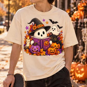 Może przedstawiać: Kremowy t-shirt z nadrukiem graficznym przedstawiającym ducha w kapeluszu czarownicy, czytającego fioletową książkę. Wzór zawiera czarnego kota, dwie dynie, zapaloną świecę, jesienne liście i małe nietoperze na tle kolorowego tła.