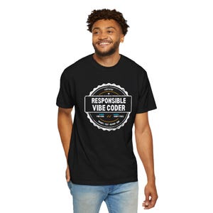 May include: A black short-sleeve t-shirt featuring a white circular graphic on the chest. The design resembles a certification seal with the text "RESPONSIBLE VIBE CODER" in the center, along with "VIBE CODER", "VERIFY TWICE", and "PROMPT TEST REVIEW SHIP".