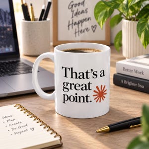 May include: A white ceramic mug filled with dark coffee, featuring the black text "That's a great point." and a small orange starburst graphic printed on the front. The mug has a standard handle and a smooth, glossy finish.