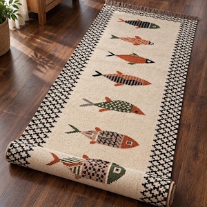 May include: A rectangular runner rug featuring a cream-colored center with seven distinct fish motifs in shades of orange, green, and black. The rug is bordered by a black and white geometric diamond pattern and has fringed ends.