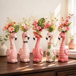 May include: Five pink flamingo-shaped ceramic vases, each holding a unique arrangement of artificial flowers. The flamingos feature varied patterns including stripes, polka dots, and floral motifs, with some wearing accessories like a straw hat or bow tie.