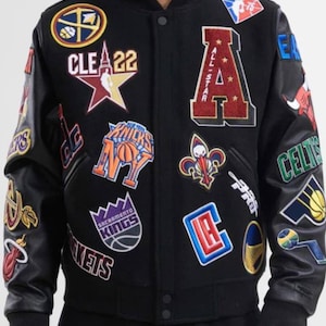 Puede incluir: Una chaqueta universitaria negra con mangas largas negras y una variedad de parches bordados coloridos que representan varios equipos de baloncesto profesional, incluyendo logotipos de los Knicks, Kings y un emblema All-Star.