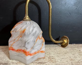 Peut inclure: Une applique murale composée d'un bras en laiton courbé et d'un abat-jour en verre en forme de cloche. L'abat-jour présente une base blanche avec des motifs marbrés gris et orange vif, fixé à une plaque de montage murale circulaire en laiton.