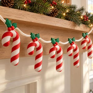 May include: A holiday garland featuring a series of red and white striped candy canes connected by a white cord. Each candy cane is topped with a pair of green holly leaves and two small red berries, creating a festive decorative string.