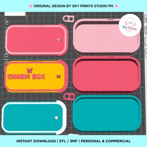 May include: A set of rectangular storage boxes with rounded corners, shown in pink, yellow, and teal. The yellow box features the text CHARM BOX with a butterfly icon. The boxes have a sliding lid mechanism and are displayed on a grid background.