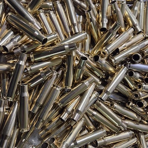 May include: A large collection of polished brass metallic cartridge casings scattered in a pile. Each individual casing features a cylindrical body with a tapered neck and an open top, showcasing a reflective gold-toned finish throughout the group.
