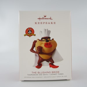 May include: Hallmark Keepsake Christmas ornament featuring the Tasmanian Devil from Looney Tunes dressed as a blushing bride in a white chef's hat and apron. The ornament is red, brown, and white.