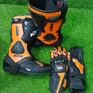 May include: A pair of black and orange motorcycle boots with KTM branding and a pair of matching black and orange motorcycle gloves. The boots feature a size label showing EUR 41, UK 7, and USA 8. Both items are designed for racing and protection.
