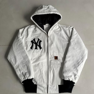 May include: A white hooded jacket featuring a black New York Yankees logo on the chest, a full-length front zip, black ribbed cuffs, and a black interior lining. A small rectangular brown brand patch is visible on the front pocket area.
