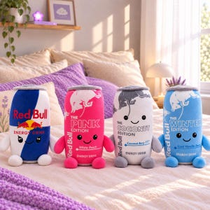 May include: Four plush toys shaped like Red Bull energy drink cans. The first is blue and silver, the second is pink, the third is white and grey, and the fourth is light blue. Each plush features a smiling face, small arms, and legs.