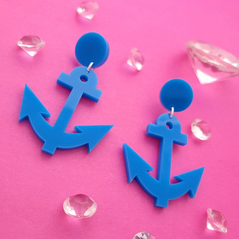 May include: A pair of bright blue anchor-shaped earrings. Each earring features a solid circular stud top connected to a flat, nautical anchor pendant. The design is uniform in color and shape, showcasing a smooth, matte finish on both pieces.