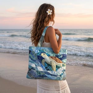 Puede incluir: Un bolso tote acolchado con un gráfico detallado de una tortuga marina sobre un mosaico de parches de tela en tonos azules y turquesas. El bolso tiene dos correas para el hombro, forma rectangular y una textura cosida en toda la superficie.