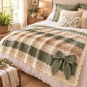 May include: A cream and sage green crocheted blanket featuring horizontal stripes, intricate lace-like patterns, and a scalloped edge. A large, matching sage green crocheted bow is attached to the lower right corner of the blanket, which is draped over a bed.