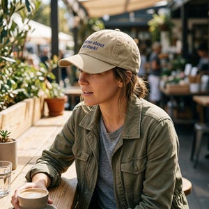 May include: A beige baseball cap with a curved brim and the text "Ask me about my stack!" embroidered in dark blue on the front. The cap features a structured crown, a button on top, and eyelets for ventilation, providing a classic athletic look.