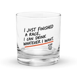 May include: A clear glass tumbler featuring the black printed text I JUST FINISHED A RACE, I CAN DRINK WHATEVER I WANT. Below the text is a horizontal orange line, the letters LN4, and a small black smiley face icon centered at the bottom.