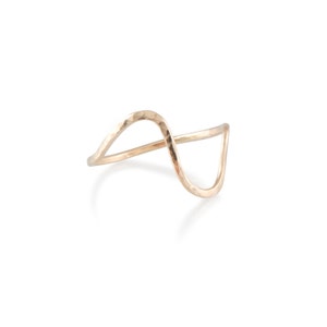 May include: A hammered gold ring with a wavy design. The ring is made of a single piece of metal that is bent into a wave shape.
