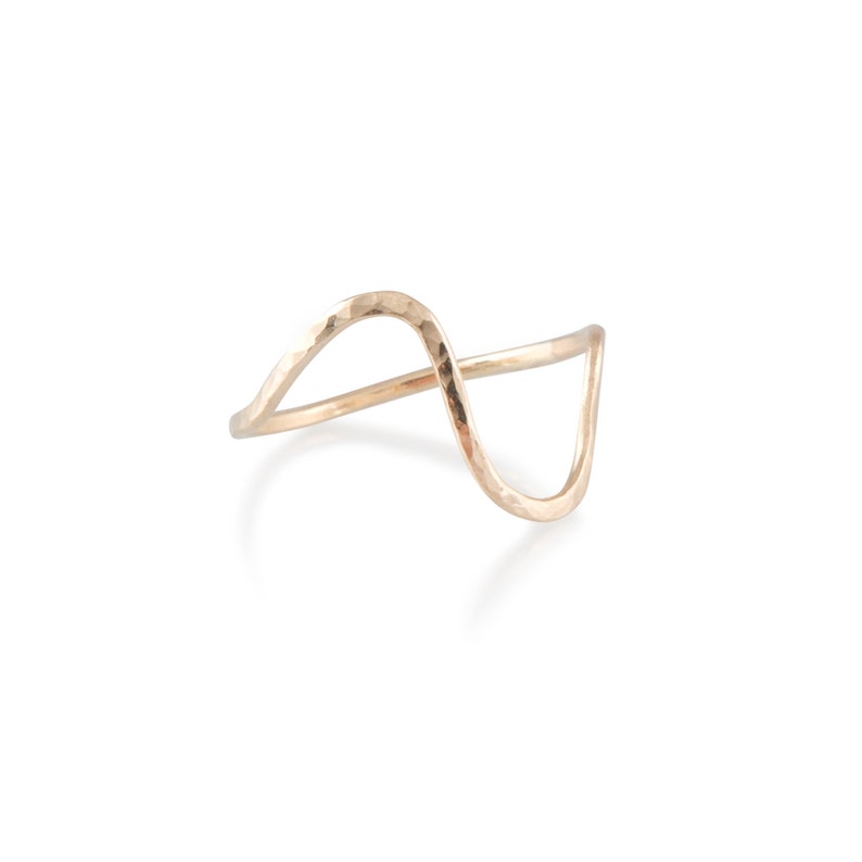 May include: A hammered gold ring with a wavy design. The ring is made of a single piece of metal that is bent into a wave shape.