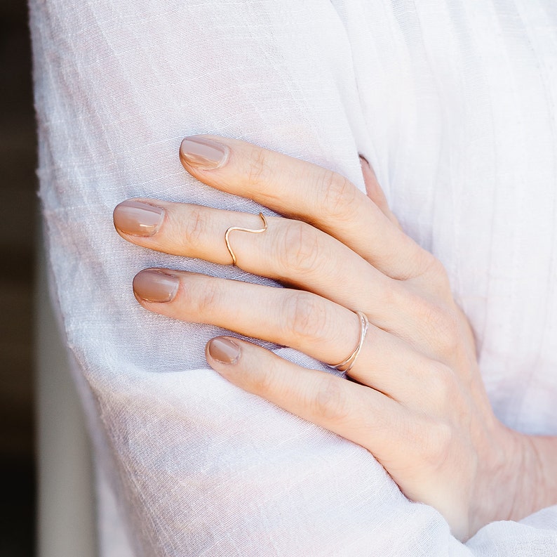 May include: A hand wearing two gold rings on the ring finger. The nails are painted a light brown color.