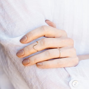 May include: A hand wearing two gold rings. The ring on the index finger is a thin, wavy band. The ring on the middle finger is a simple, thin band.