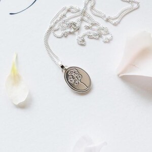 May include: A silver necklace with a delicate oval pendant featuring a floral design. The pendant is engraved with a stylized flower.