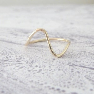 May include: A gold-toned ring with a wavy, hammered design. The ring is open and has a simple, minimalist style.
