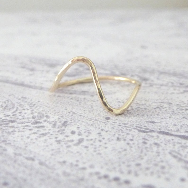 May include: A gold-toned ring with a wavy, hammered design. The ring is open and has a simple, minimalist style.