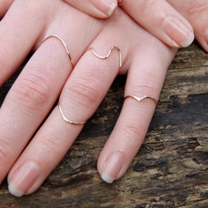 May include: A set of four gold-toned rings, each with a unique design. The rings are worn on the fingers of a hand, with the rings stacked on top of each other.